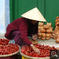 In Vietnam’s streets bustle everywhere fly-pitchers with typical head covering. Mostly are food or fruit offered, less frequent souvenirs like here. Photo: S. Elser.